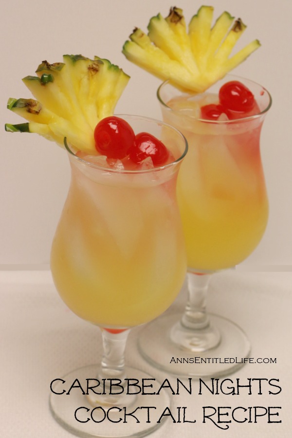 Two hurricane glasses filled with Caribbean Nights cocktail, garnished with pineapple and cherries againstb a tan background