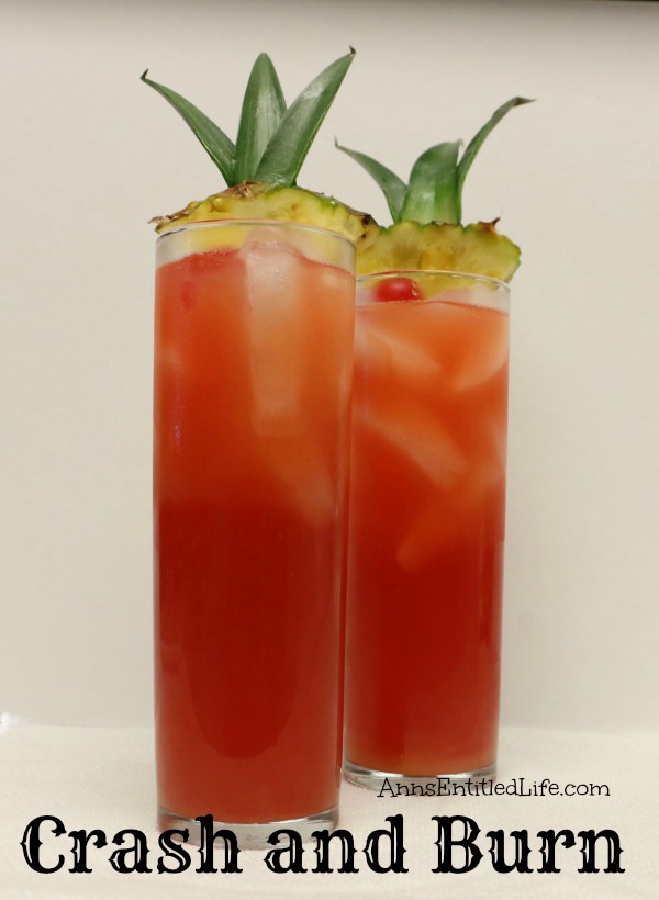 Two crash and burn cocktails in tall glasses garnished with pineapple and cherries against a white background