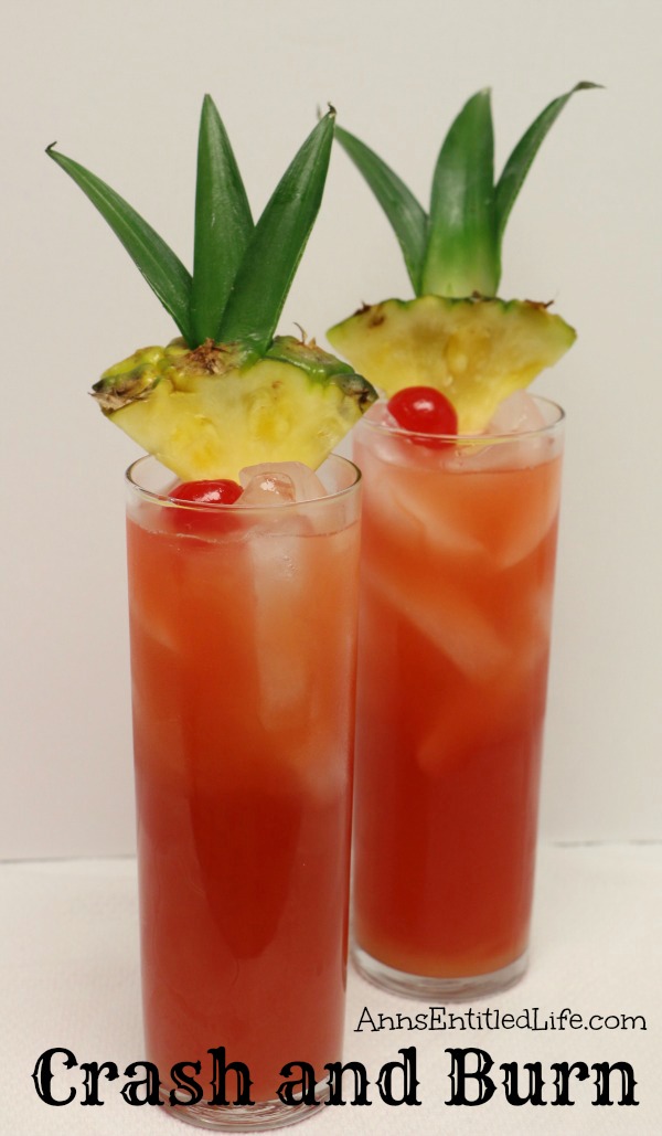 Two crash and burn cocktails in tall glasses garnished with pineapple and cherries against a white background