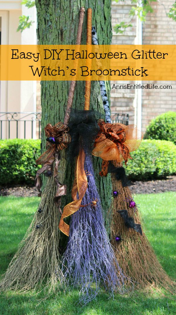 3 decorated witch's brooms leaning against a tree, house and gardens in background