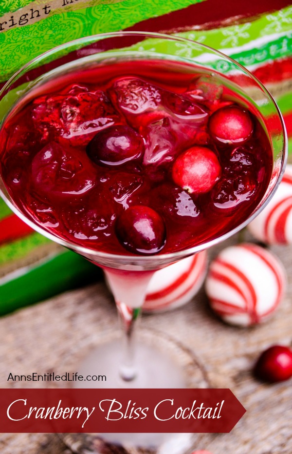 An overhead view of a martini glass filled with a cranberry cocktail standing against a red and green background. There are red and white holiday balls in the lower right.
