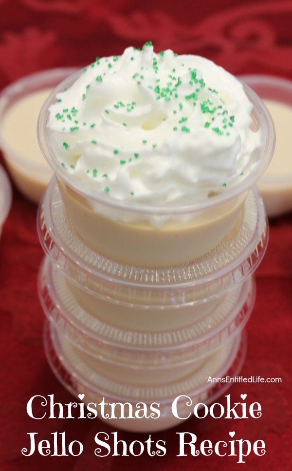a stack of Christmas cookie jello shots stacked in souffle cups, the top one is open and covered in whipped cream and sprinkles, surrounded by more Christmas cookie jello shots, sitting on a red placemat