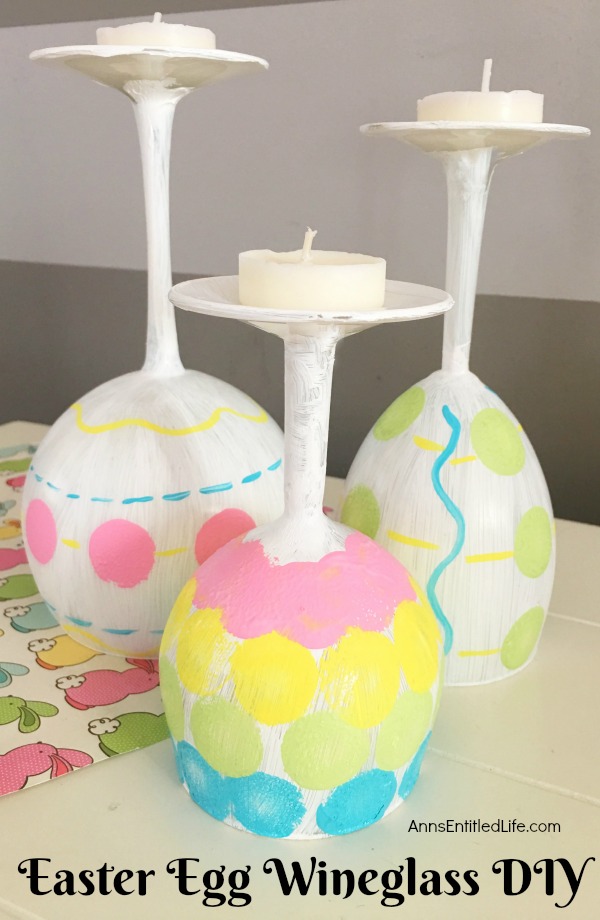 Three wine glasses painted to resemble Easter eggs sitting on a bunny matt.