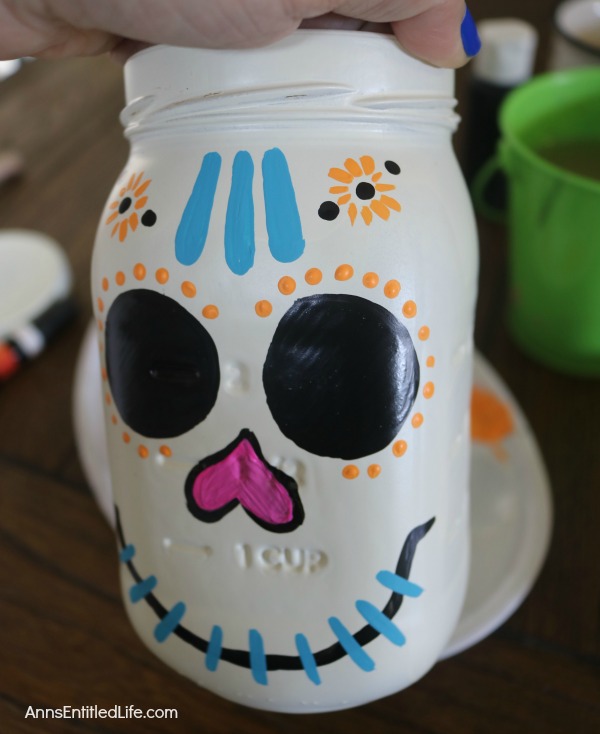 Sugar Skull Mason Jar Craft. This easy to make sugar skull is fashioned from an old Mason jar.  You can store kitchen utensils, candy (keep the lid!), etc in these jar for Halloween or to celebrate the Day of the Dead. Using old glass jars is a great way to get crafty at home and make your own cute décor at the same time.