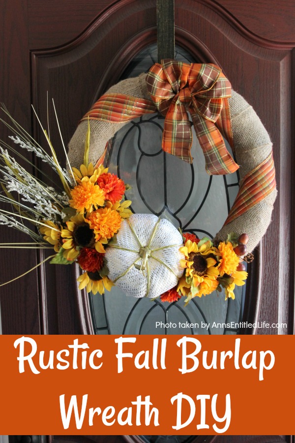 Burlap wreath with a ribbon on the top, the bottom is a white pumpkin, wheat, and seasonal floral. This is hanging on a wood and glass door.