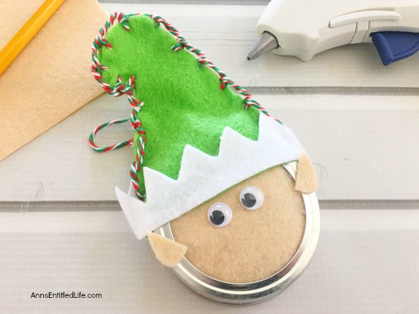 Elf Mason Jar Lid Ornament DIY. This easy to make Elf Mason jar lid ornament is simply adorable. This step by step tutorial has easy to follow directions so you can make one for your tree, to give as a gift, or to place on top of a present as a little something extra.