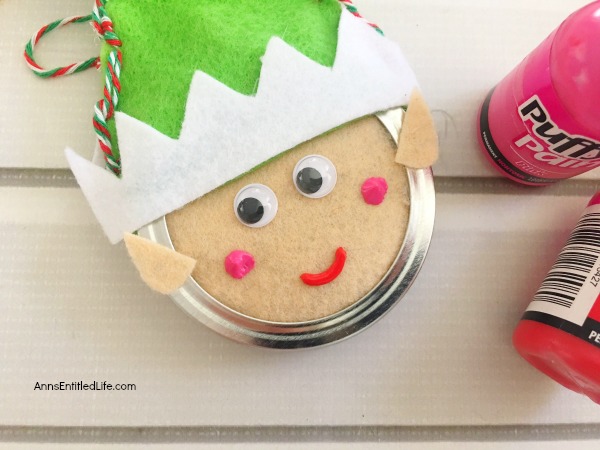 Elf Mason Jar Lid Ornament DIY. This easy to make Elf Mason jar lid ornament is simply adorable. This step by step tutorial has easy to follow directions so you can make one for your tree, to give as a gift, or to place on top of a present as a little something extra.