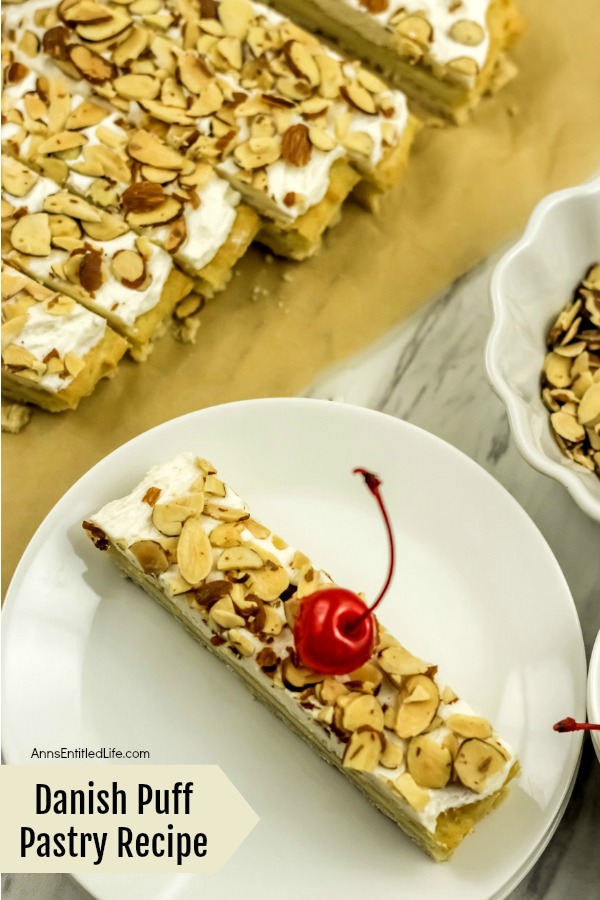 overhead view of a piece of Danish pastry puff on a white plate surrounded by the rest of the Danish puff and a bowl of almonds