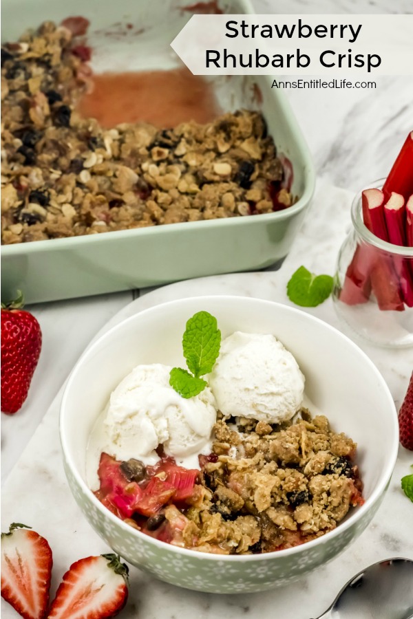 white bowl with a serving of strawberry rhubarb crisp topped with vanilla ice cream, the pan filled with strawberry rhubarb crisp is in the upper left, a glass filled with rhubarb is in the upper right, cut strawberries surround the dishes