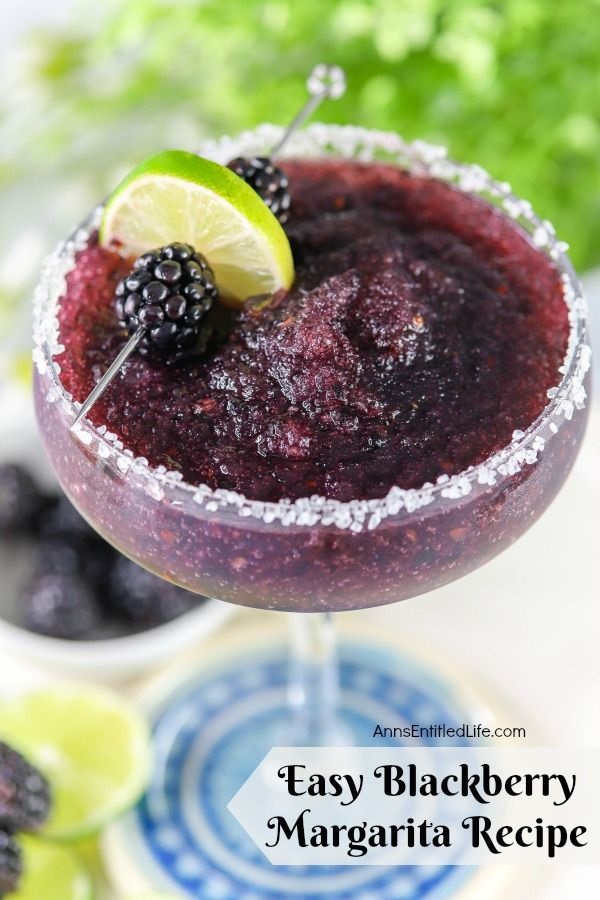 Overhead view of a blackberry margarita in a glass, a lime and fresh blackberry garnish on a skewer lays across the back. Below is a bowl of fresh blackberries