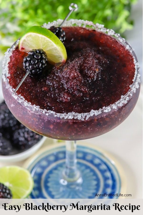 Overhead view of a blackberry margarita in a glass, a lime and fresh blackberry garnish on a skewer lays across the back. Below is a bowl of fresh blackberries