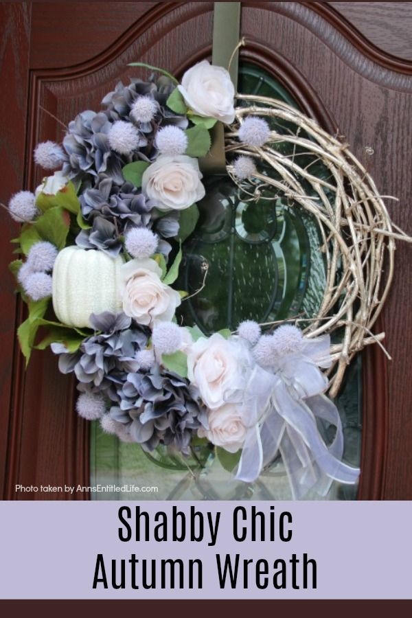 A beautiful fall wreath in colors of grey, blush, and white on a grapevine wreath, hanging on a brown door with a glass insert