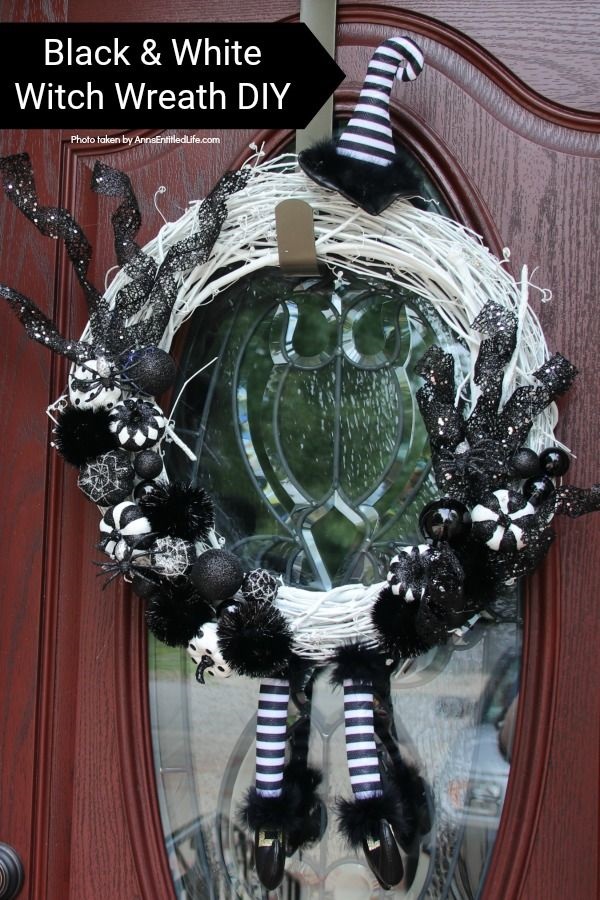 A Halloween wreath done in black and white hanging from a copper wreath hanger against a glass and brown door.