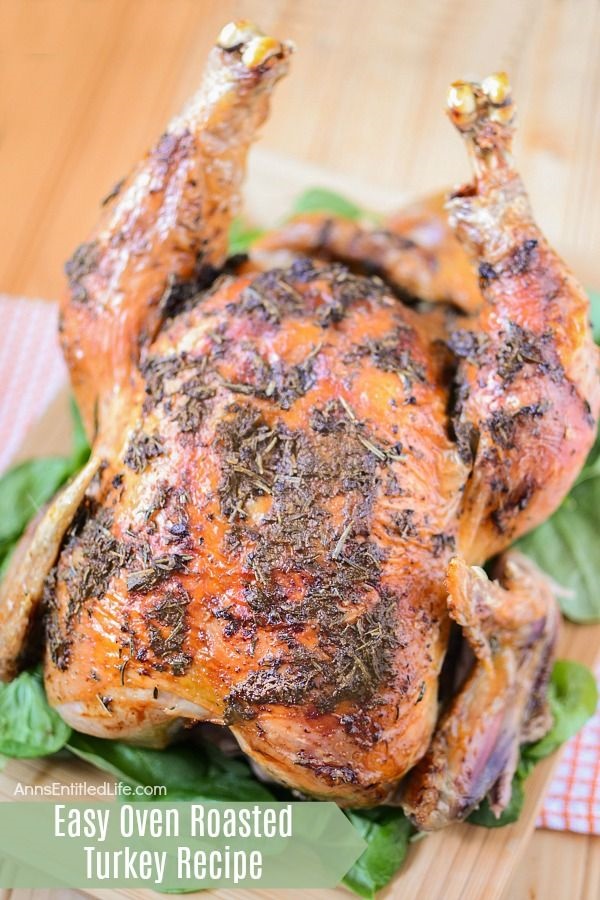 A whole, cooked turkey covered in herbs, sitting on a bed of lettuce on a cutting board.