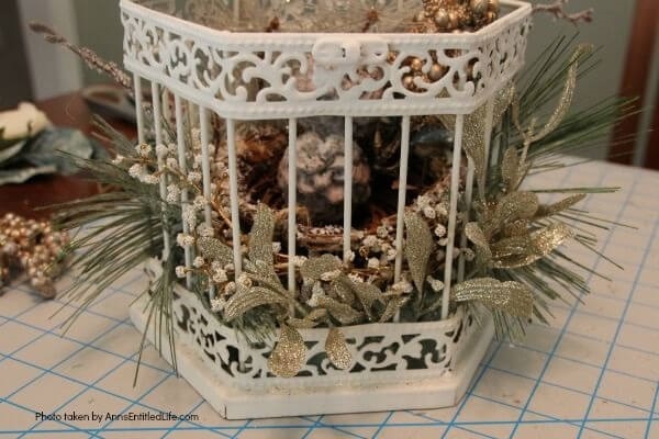 Have an old birdcage lying about that you would like to repurpose into a beautiful decor piece? This wonderful winter white birdcage decorating idea is a lovely DIY decorating piece for the holidays and beyond. This tells the story of a bird that has left the cage to fly south for the winter. His (or her) nest is empty, and he (or she) is off to parts unknown. This is not only a lovely winter piece, it could be used for wedding decor, a centerpiece, a front foyer piece (I always decorate my foyer!) or you could hang it as an empty birdcage in a Florida room or family room.