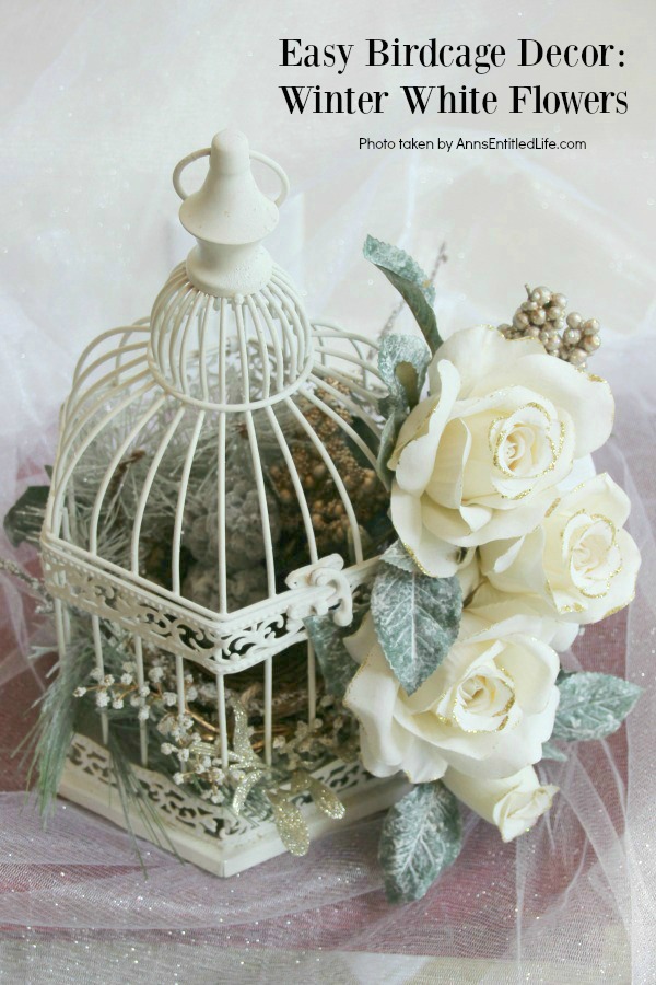 A white bird cage decorated with faux white flowers and greenery against a white background