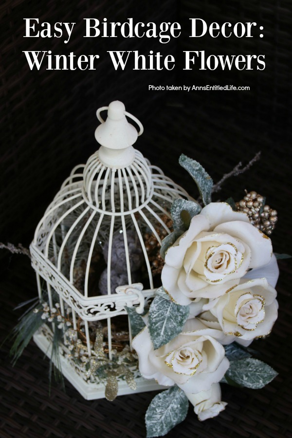 A white bird cage decorated with faux white flowers and greenery against a black background