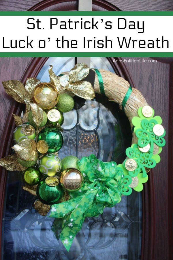 straw wreath decorated for st patrick's day with green and gold bulbs, green ribbon, and gold coins, hanging on a bronze door hanger against a window on a brown door