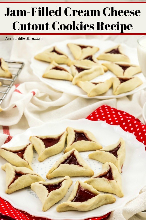 An side-view of two white plates willed with jam cookies (triangular shaped cookies with jam in the middle). A rack has more jam cookies in the upper left. There is a glass of milk in the upper right.