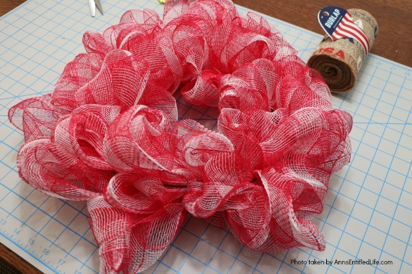 Patriotic Farmhouse Wreath DIY. This simple to make, rustic style American patriotic mesh farmhouse wreath is wonderful for outdoor or indoor display. Using only three materials and scissors, this easy to make wreath comes together in about 15 minutes. If you are looking for a patriotic holiday wreath, this little beauty is it!
