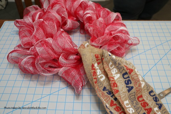 Patriotic Farmhouse Wreath DIY. This simple to make, rustic style American patriotic mesh farmhouse wreath is wonderful for outdoor or indoor display. Using only three materials and scissors, this easy to make wreath comes together in about 15 minutes. If you are looking for a patriotic holiday wreath, this little beauty is it!