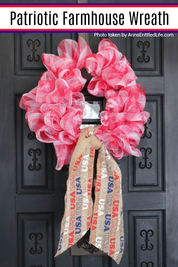 A mesh patriotic wreath with a USA burlap tie hanging on a bronze holder against a brown door.