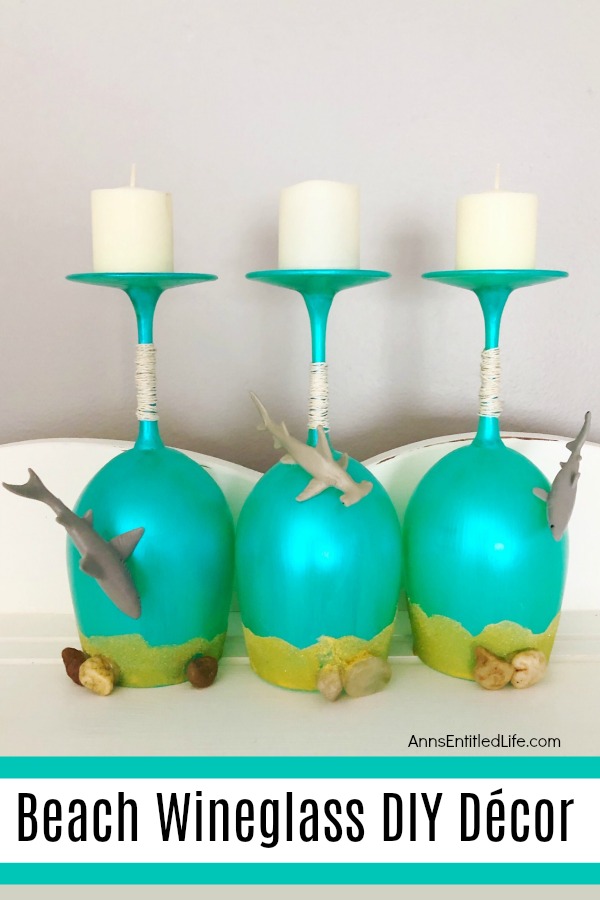 aqua painted wineglasses, upside down, with sand and pebbles embellishments on a grey background