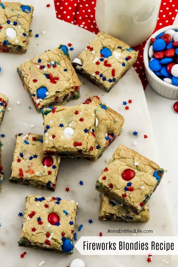 festive red, white, and blue blondies bars on a white plate, M&Ms upper right, milk glass on red polka dot napkin also in the upper right