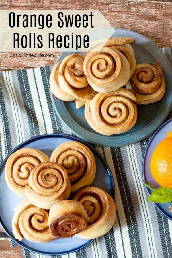 two blue plates filled with orange sweet rolls on a blue striped napkin, on a wooden background. part of a fresh orange and mint spring are shown on the bottom right