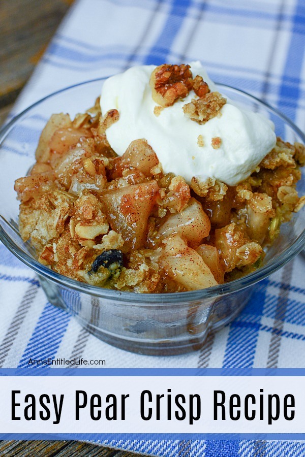 clear bowl filled with pear crisp, a dollop of whipped cream on top. There is a spoon to the right, all on top of a blue checked napkin