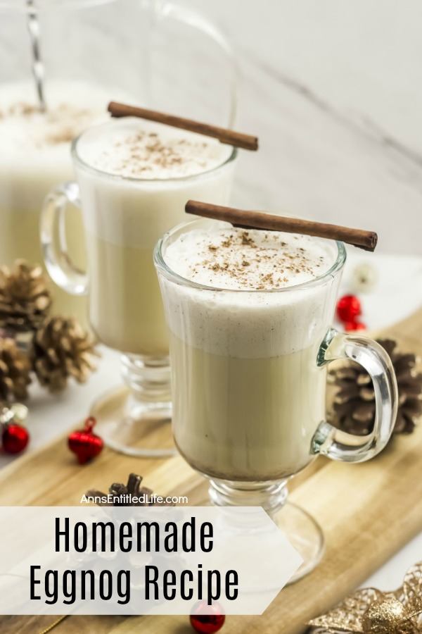 pitcher of homemade eggnog and two poured glasses on a butcher block, with pinecone and red bulbs scattered about