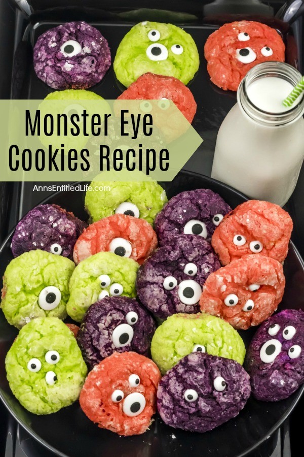 multicolored cookies with candy eyeballs on a dark tray, a bottle of milk wth a straw is in the upper right