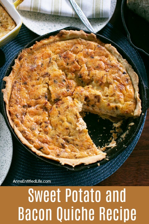 sweet potato and bacon quiche missing on slice, in a black pan, on a blue placemat. A napkin and silverware rests above the serving