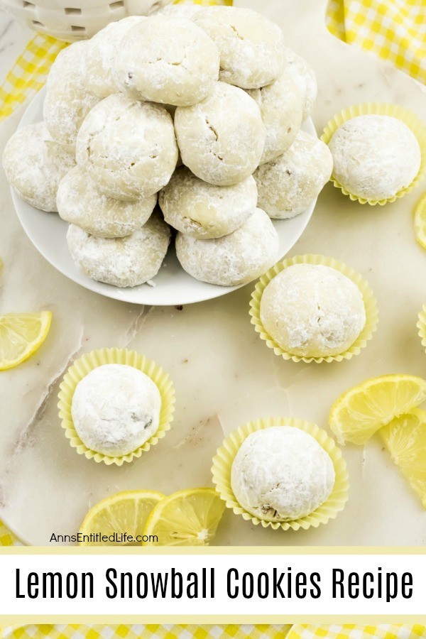 5 lempon snowball cookies in yellow cupcake holders, a white plate full of lemon snowball cookies in the upper left. Fresh lemons are displayed as garnish. All sits on a white board