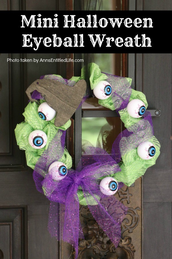 green tulle mesh wreath with purple bow and overlay, black wooden hat and hanger, hanging on a black door