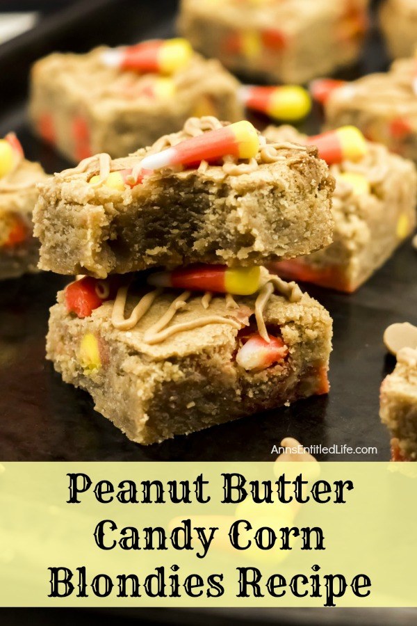 a double stack of peanut butter candy corn blondies on top of a black counter, the top blondie has a piece missing to expose the inside, dropped candy corn for garnish, and more of the blondies surrounding the stack