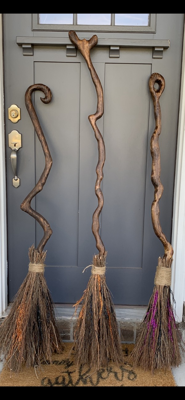 3 decorated witch's brroms leaning against a tree, house and gardens in background