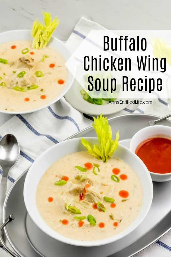  An overhead shot of a white bowl filled with Buffalo chicken wing soup set in a silver tray, a small white bowl of hot sauce next to it, a second bowl is in the upper left, a bowl of celery stalks in the upper right.