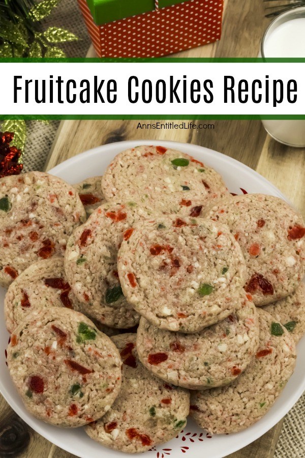 An overhead view of a holiday plate filled with fruitcake cookies cookies. Above the plate to the right is a glass of milk, directly above the plate is a gift, and a few ornaments or on the upper left.