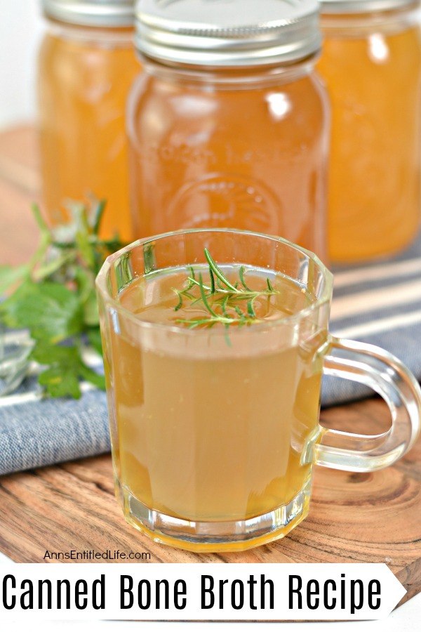 A steaming cup of bone broth with a herb sprig floating on top, three jars of canned bone broth on a blue and white striped towel in the background
