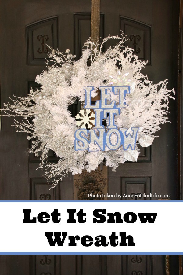 An excessively decorated white wreath (crystals, silver, rhinestones) with a let it snow sign, hanging from a bronze wreath hanger on a dark brown door.