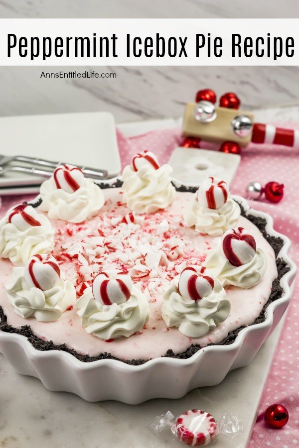 A side view of a peppermint icebox cake in a round fluted white plate decorated with peppermint candies and whipped cream. This sits on a white and pink polka dot tablecloth and is surrounded with small holiday decor and ornaments.
