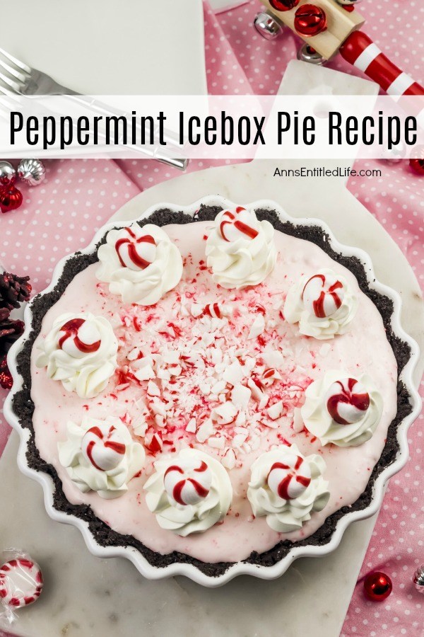 A peppermint icebox cake in a round fluted white plate decorated with peppermint candies and whipped cream. This sits on a white and pink polka dot tablecloth and is surrounded with small holiday decor and ornaments.