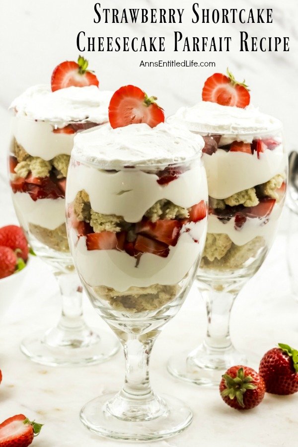 three strawberry cheesecake partfait desserts on a white background surrounded by fresh strawberries