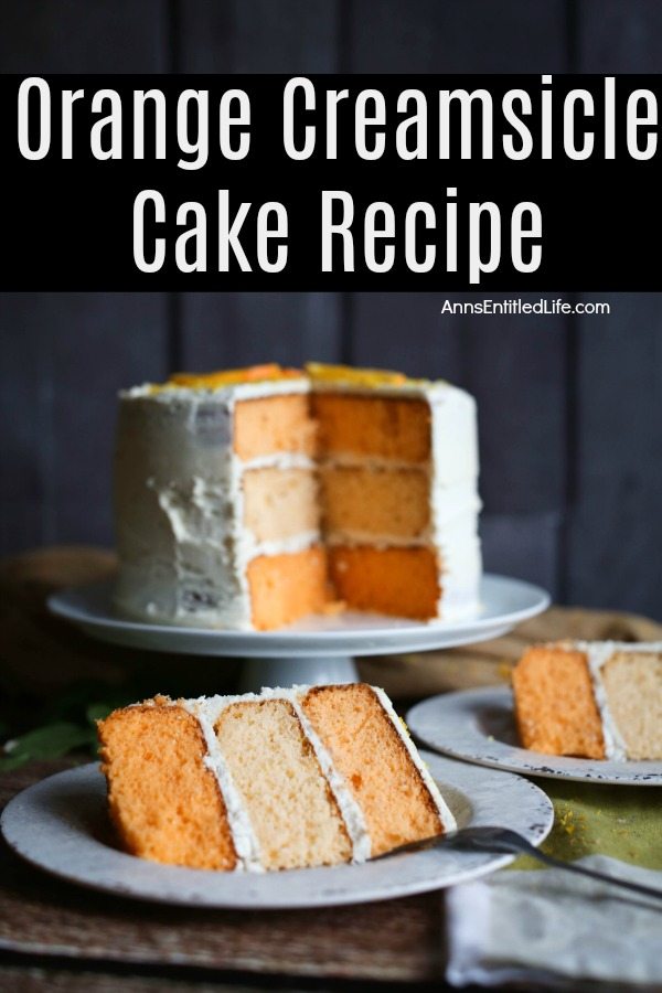 Two pieces of plated orange creamsicle cake, the remaining three-tier cake is on a white cake plate behind the pieces of served cake, front view