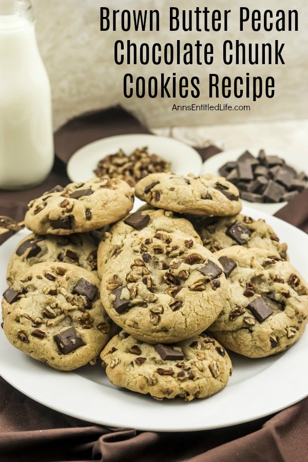 white plate filled with Brown Butter Pecan Chocolate Chunk Cookies on a brown napkin, a bowl of of pecans and chunk chips in the background, a jug of milk in the upper left