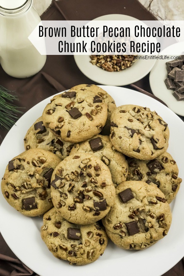 Overhead view of a white plate filled with Brown Butter Pecan Chocolate Chunk Cookies on a brown napkin, a bowl of of pecans and chunk chips in the background, a jug of milk in the upper left