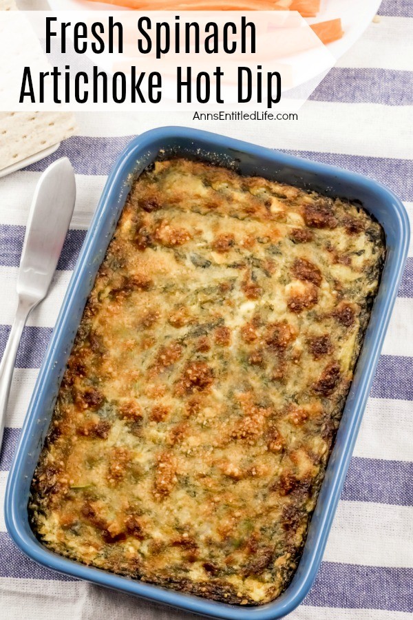 Blue pan filled with baked spinach artichoke dip, on a blue and white towel, a serving knife to the left