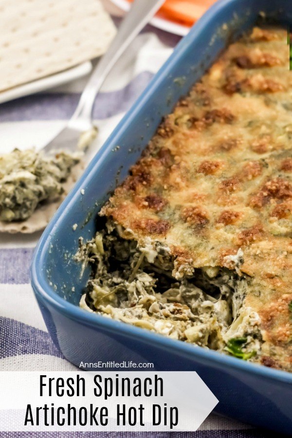 Blue pan filled with baked spinach artichoke dip, one portion removed, on a blue and white towel, the removed portion is to the left on a serving knife