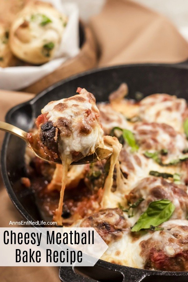 A forkful of cheesy meatballs being lifted from a skillet pan. A basket of knot rolls are seen in the back left.